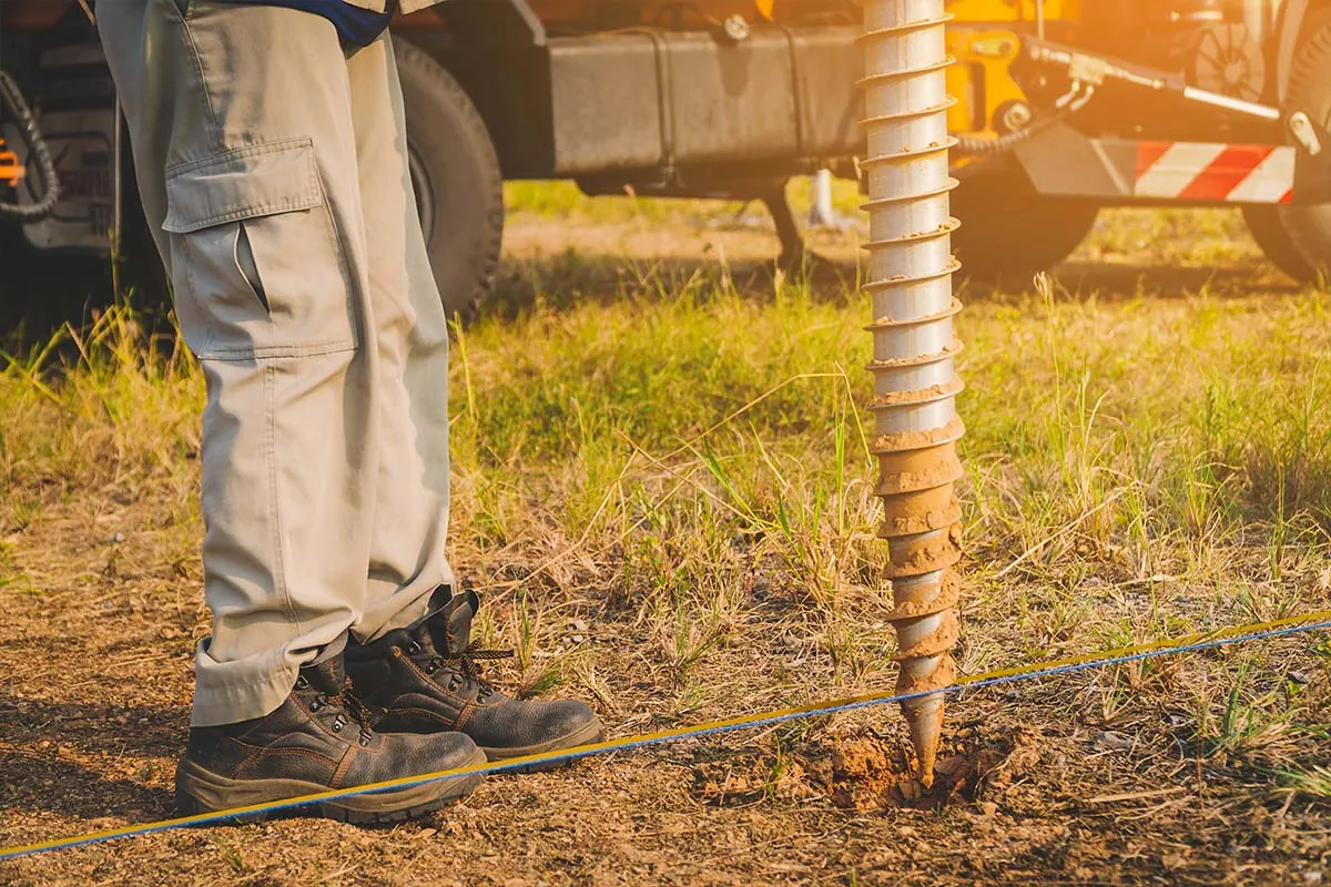 Ground screw being installed with workers on site