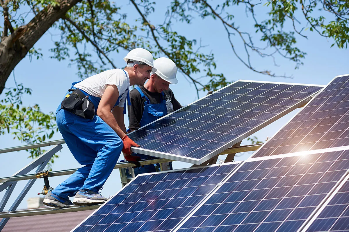 Solar installers in hard hats mounting a panel onto a steel racking frame